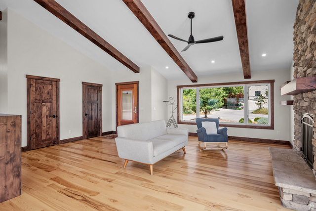 4221 Juniper Circle Alpine, UT 84004 - Photo 7 of 66 Vaulted ceilings featuring exposed wood beams, a stone-clad fireplace with a stone hearth, expansive windows with wood trim, wood-finish flooring, and dark wood paneled doors