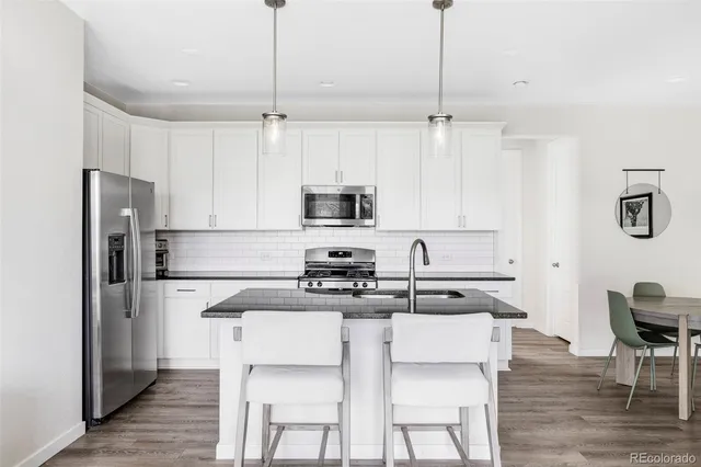 a kitchen with stainless steel appliances granite countertop a dining table chairs refrigerator and sink