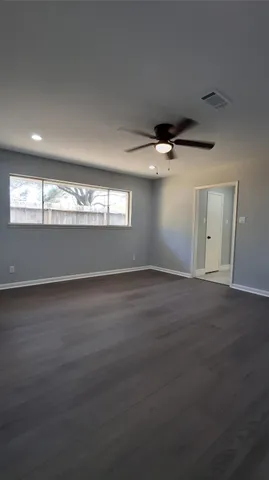 an empty room with wooden floor fan and windows
