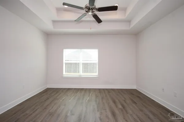 an empty room with wooden floor ceiling fan and windows