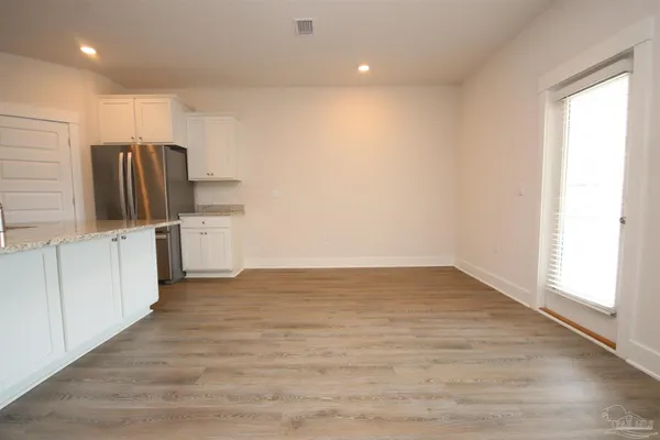 an empty room with wooden floor and a kitchen