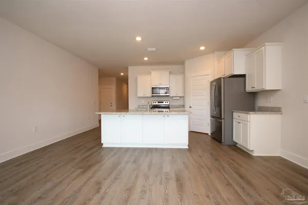 a kitchen with stainless steel appliances granite countertop a refrigerator a stove top oven a sink and white cabinets with wooden floor