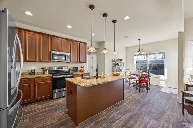 a kitchen with stainless steel appliances granite countertop a stove top oven a sink dishwasher a dining table and chairs with wooden floor