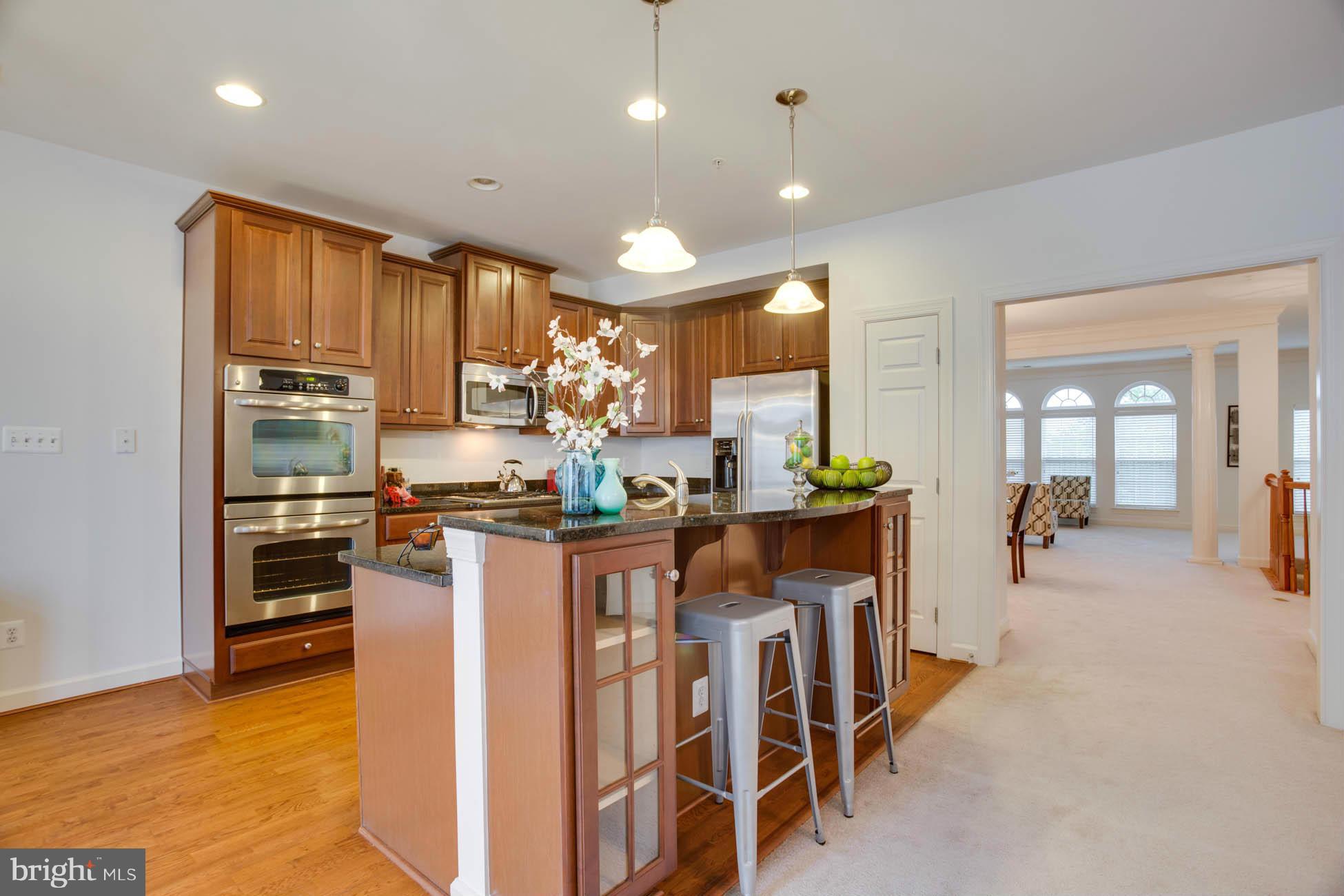 5723 Callcott Way, Unit M Alexandria, VA 22312 - Photo 15 of 28 a kitchen with stainless steel appliances kitchen island granite countertop a stove a refrigerator a sink a dining table and chairs with wooden floor