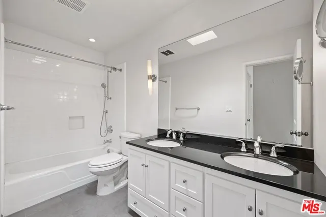 a bathroom with a granite countertop double vanity sink large mirror bathtub and shower