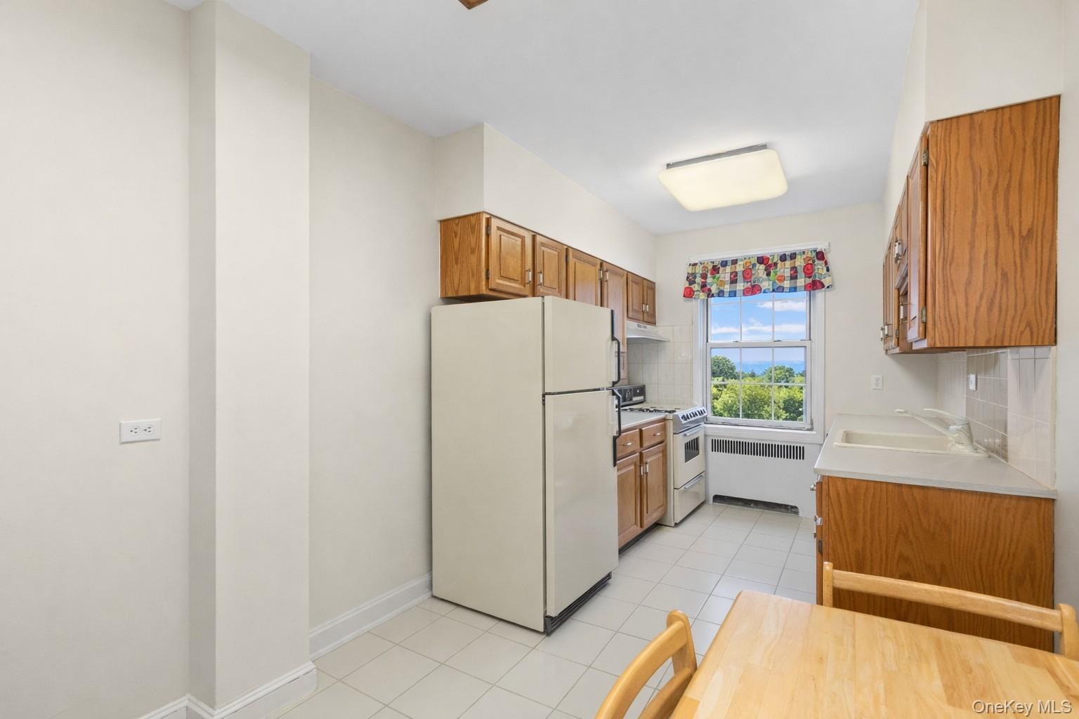 60 Pinewood Road, Unit 1B Hartsdale, NY 10530 - Photo 11 of 27 Eat-in-kitchen featuring cream appliances, light countertops, tasteful backsplash and wood cabinetry.