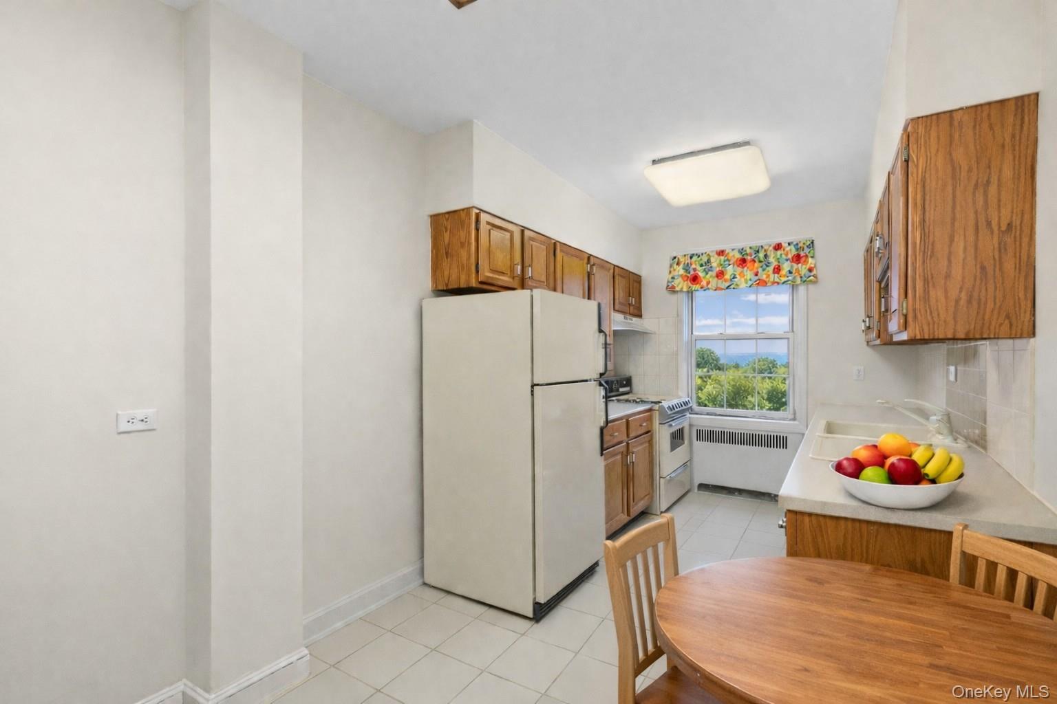 60 Pinewood Road, Unit 1B Hartsdale, NY 10530 - Photo 10 of 27 Virtually staged eat-in-kitchen featuring cream appliances, wood cabinetry, tasteful backsplash, and light tile patterned floors.