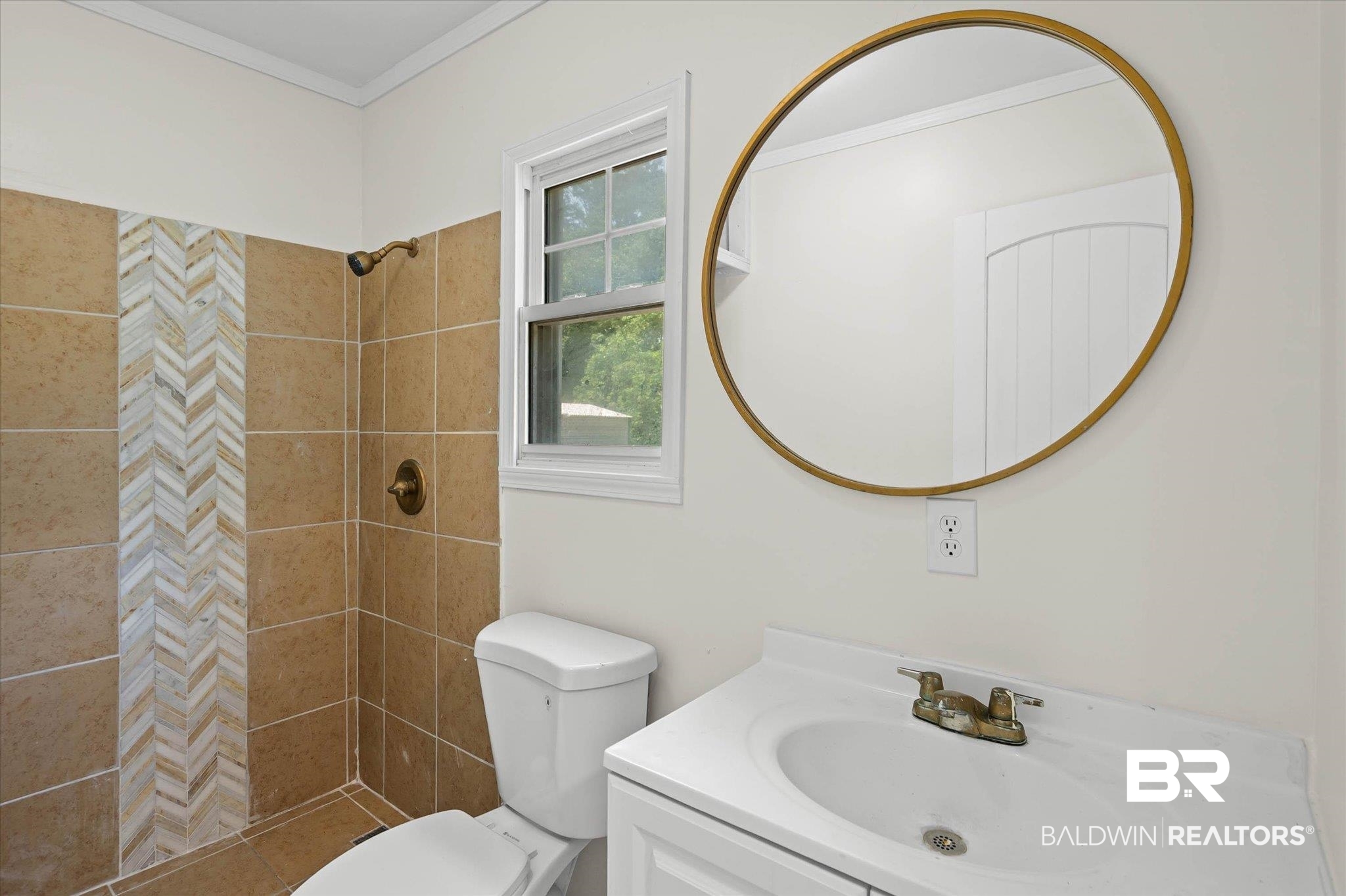 9230 McLeod Road Mobile, AL 36695 - Photo 17 of 20 Bathroom featuring a shower with herringbone tile accent, a white vanity with an integrated sink, a round gold-framed mirror, and a window providing natural illumination