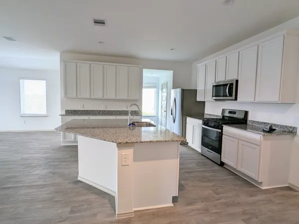 a kitchen with stainless steel appliances granite countertop a stove top oven a refrigerator a sink and dishwasher with wooden floor