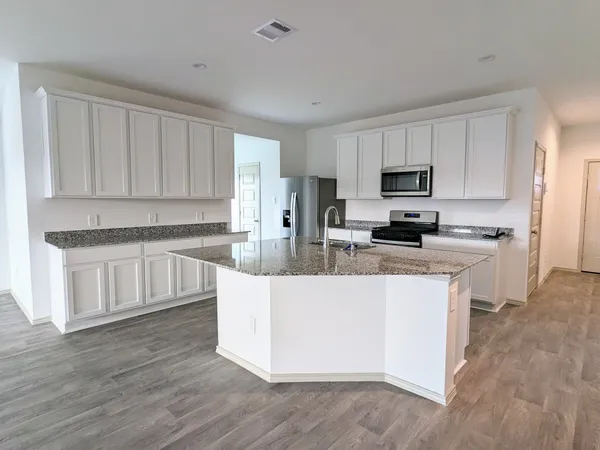 a kitchen with kitchen island granite countertop white cabinets a sink a stove a refrigerator and dishwasher with wooden floor