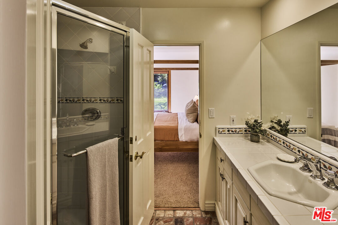 6138 Ramirez Canyon Road Malibu, CA 90265 - Photo 15 of 31 a en suite bathroom with a sink a mirror and a shower
