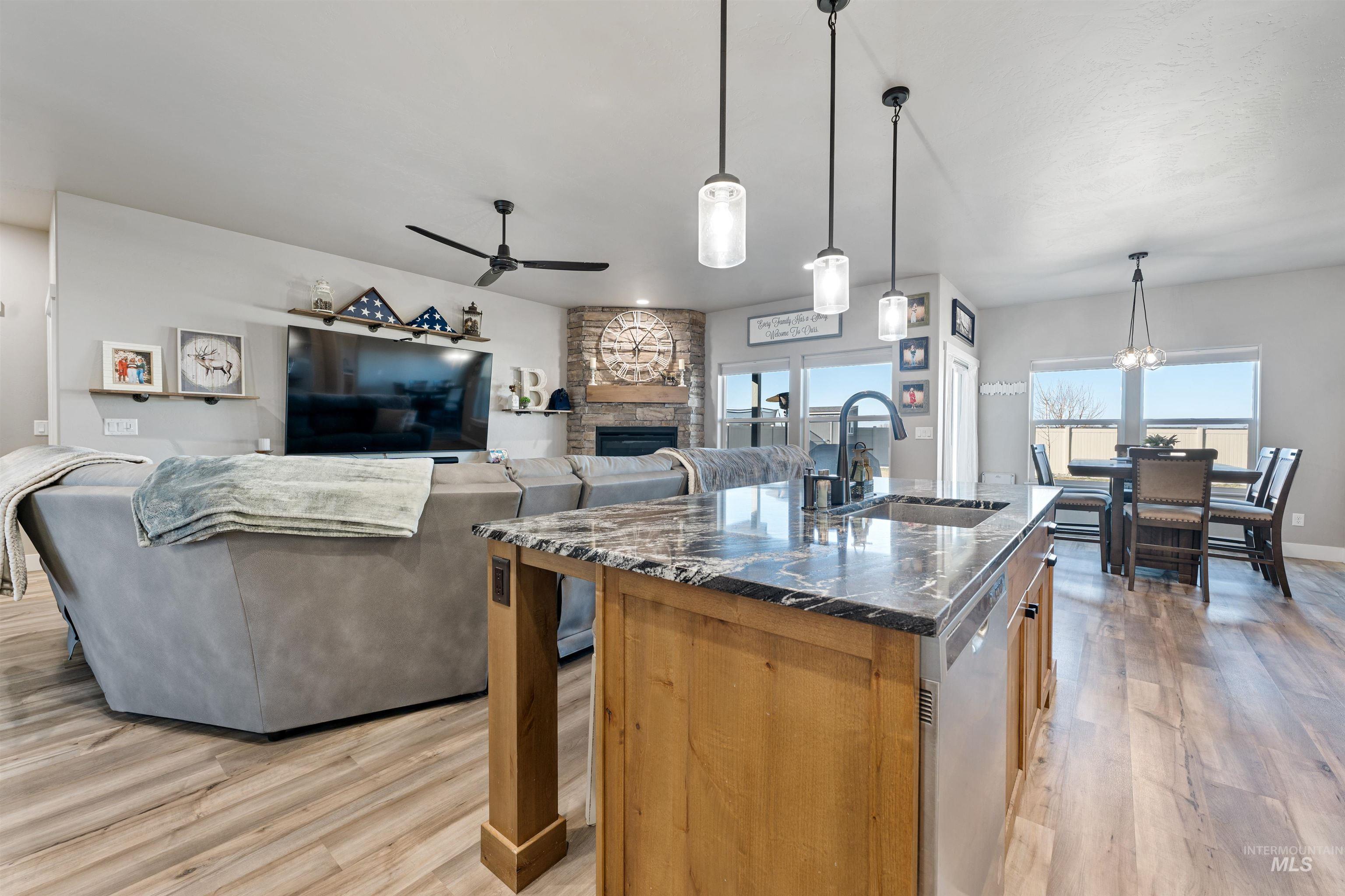 1005 Kenbrook Loop Twin Falls, ID 83301 - Photo 9 of 47 Kitchen featuring a stone fireplace, hanging light fixtures, light wood finished floors, a center island with sink, and ceiling fan
