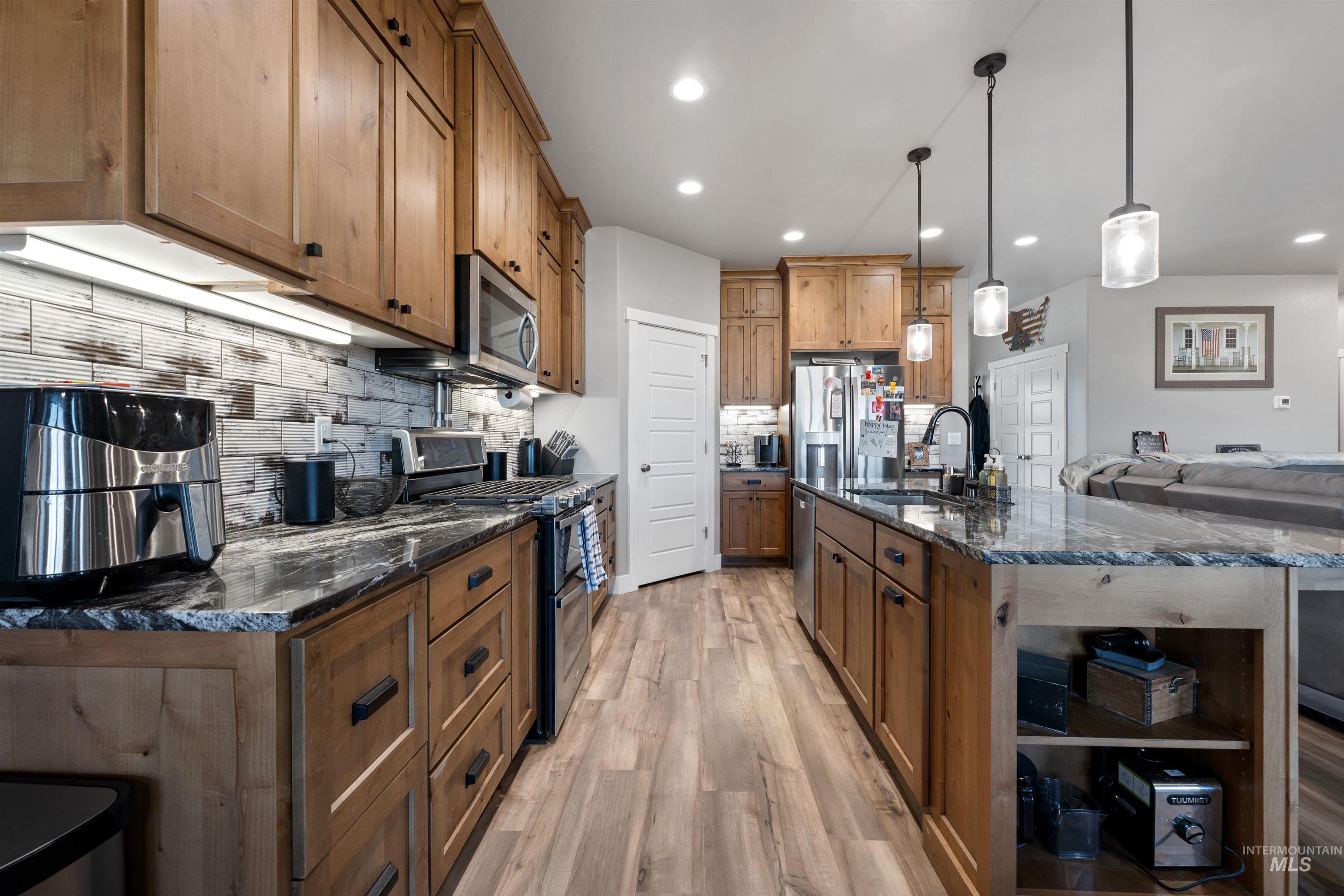 1005 Kenbrook Loop Twin Falls, ID 83301 - Photo 46 of 47 Kitchen featuring decorative backsplash, dark stone counters, stainless steel appliances, pendant lighting, and open floor plan