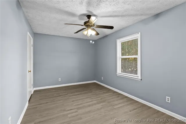 an empty room with wooden floor chandelier fan and windows