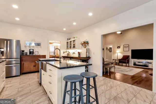 a kitchen with stainless steel appliances granite countertop a sink a stove a refrigerator and chairs