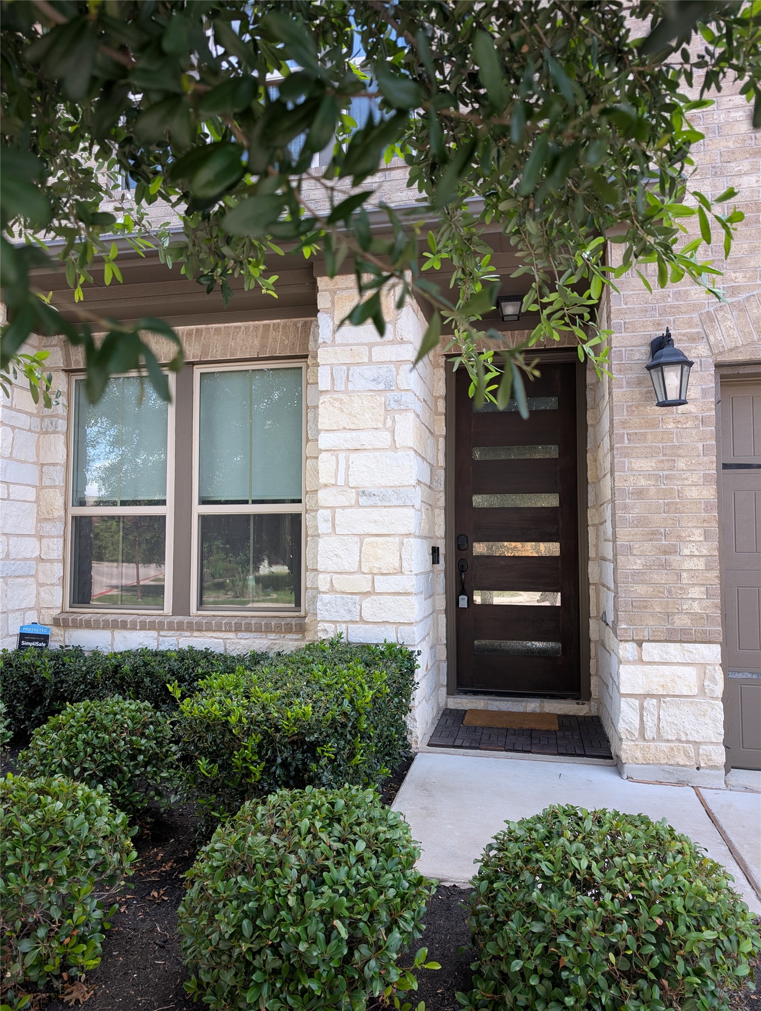 14502 McCoy Loop Austin, TX 78717 - Photo 2 of 26 Front entry featuring a modern dark wood door with horizontal glass panels, stone and brick facade, a concrete walkway, and established front yard landscaping with shrubs
