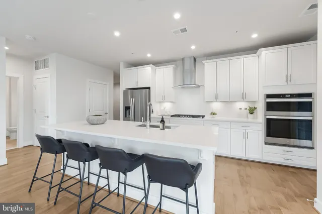 a kitchen with stainless steel appliances a sink a stove a refrigerator with white cabinets and wooden floor