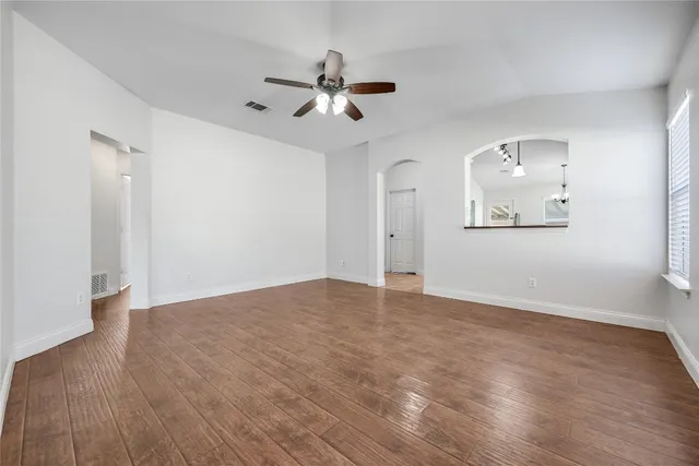 a view of an empty room with wooden floor and a ceiling fan