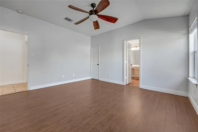 an empty room with wooden floor ceiling fan and windows