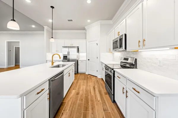 a kitchen with stainless steel appliances a stove a sink a refrigerator a microwave oven a stove and white cabinets with wooden floor