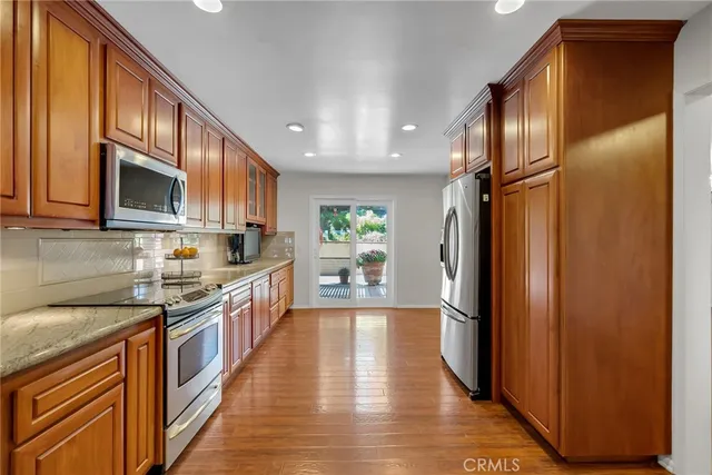 a kitchen with stainless steel appliances granite countertop a refrigerator a stove top oven a sink and dishwasher with wooden floor