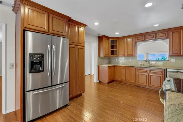 a kitchen with stainless steel appliances granite countertop a refrigerator a stove and a sink with wooden floor