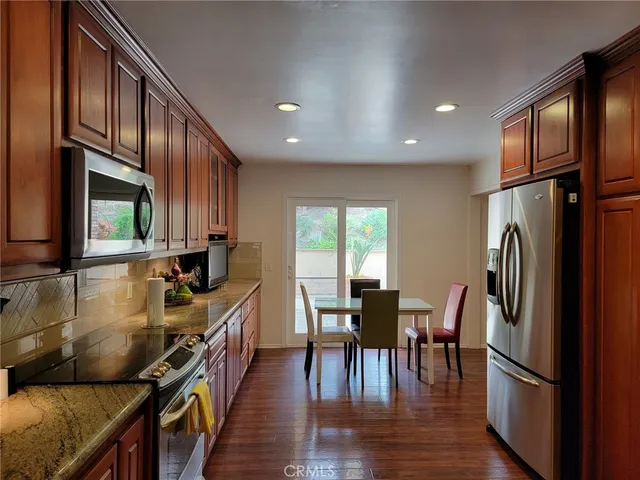 a kitchen with stainless steel appliances granite countertop a refrigerator a stove a sink dishwasher a dining table and chairs with wooden floor