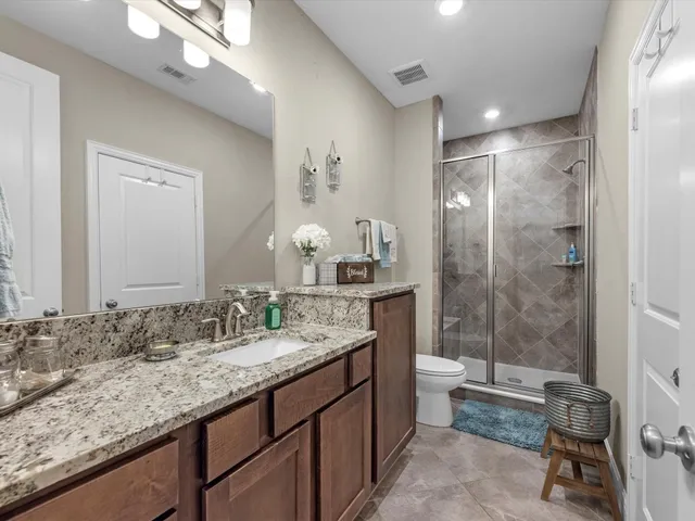 a bathroom with a granite countertop sink a toilet a mirror and shower
