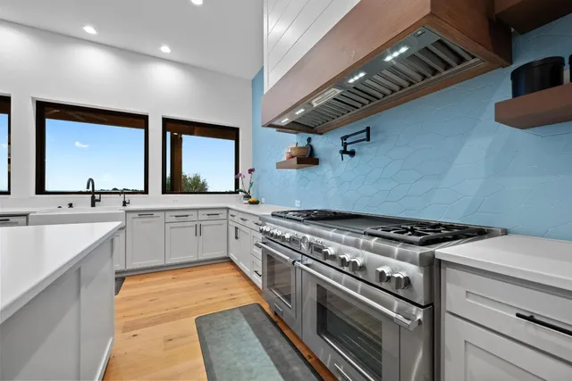 a white kitchen with stainless steel appliances granite countertop a stove and a sink