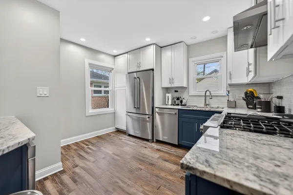 a kitchen with granite countertop a stove a sink dishwasher a refrigerator and wooden cabinets with wooden floor