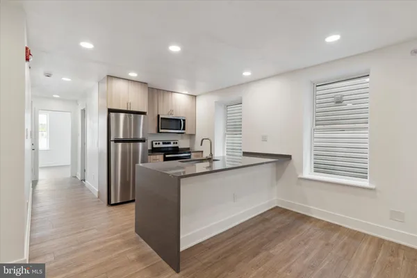 a kitchen with stainless steel appliances granite countertop a refrigerator a sink dishwasher a stove and white countertops with wooden floor