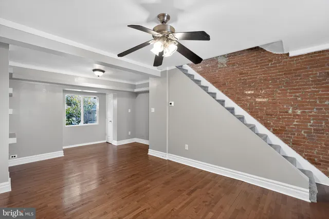 a view of an empty room with wooden floor and a ceiling fan