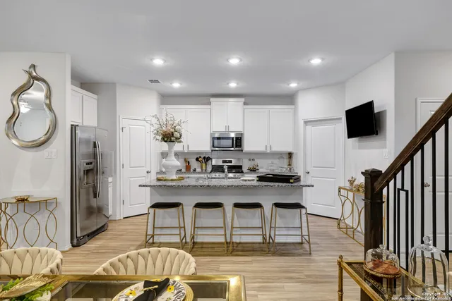 a kitchen with stainless steel appliances granite countertop a sink a stove a refrigerator cabinets and a dining table with wooden floor