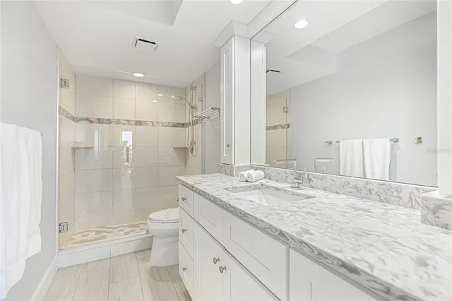 a bathroom with a granite countertop sink a toilet a mirror and shower