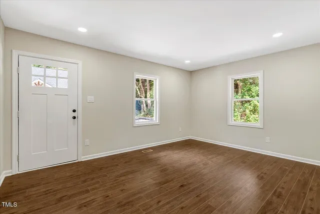 a view of an empty room with wooden floor and a window