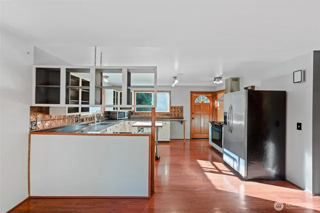a kitchen with stainless steel appliances granite countertop a refrigerator a stove and a sink with wooden floor