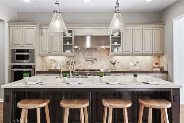 a kitchen with stainless steel appliances a stove a sink island and chairs in it