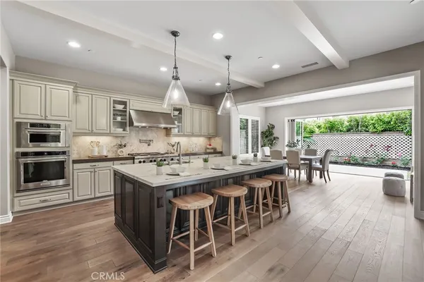 a kitchen with stainless steel appliances granite countertop a stove top oven a refrigerator a sink dishwasher and a dining table with wooden floor