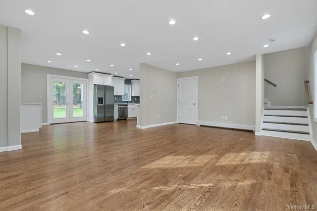 a view of an empty room with wooden floor kitchen and windows