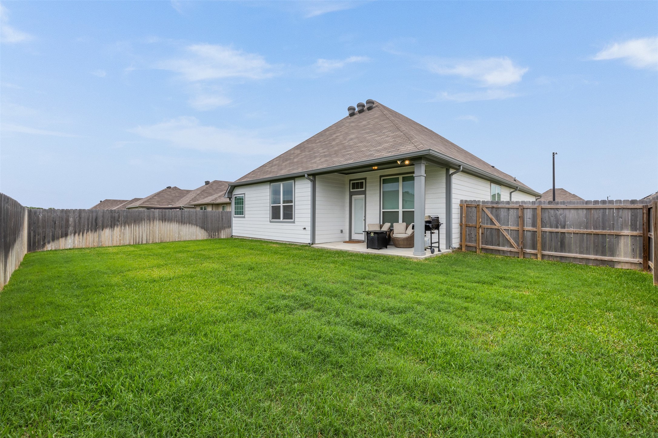 1968 Chief Street Bryan, TX 77807 - Photo 17 of 27 This photo showcases a backyard with a spacious grassy area, enclosed by a wooden fence. There's a covered patio attached to the house, featuring outdoor seating and a grill, ideal for relaxation and entertaining.