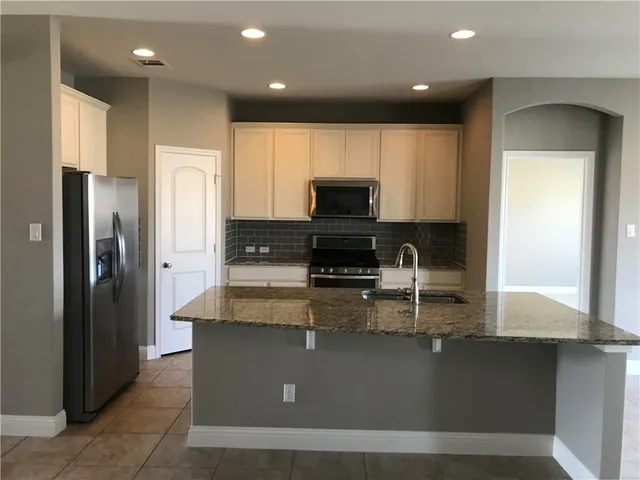 a kitchen with kitchen island granite countertop a refrigerator a stove a sink and a microwave