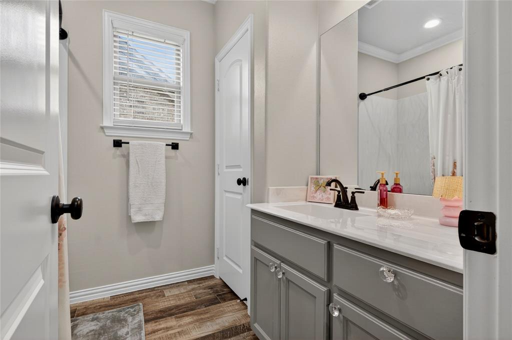 701 West Lamberth Road Sherman, TX 75092 - Photo 27 of 37 Bathroom with wood-finish flooring, a single window with blinds, and a vanity featuring a white countertop and gray cabinetry with clear knob hardware