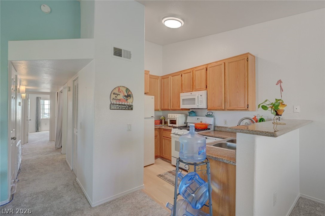 3318 North Decatur Boulevard, Unit 2072 Las Vegas, NV 89130 - Photo 13 of 50 A compact kitchen with warm wooden cabinetry and granite counters overlooks a plush carpeted hallway.