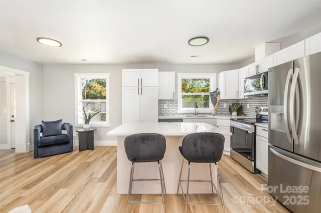 a kitchen with stainless steel appliances granite countertop a refrigerator a stove a dining table and chairs with wooden floor