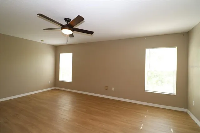 an empty room with wooden floor fan and windows