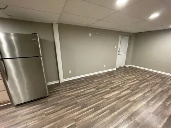 a view of an empty room with wooden floor and a refrigerator