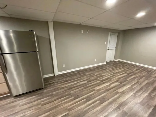 a view of an empty room with wooden floor and a refrigerator