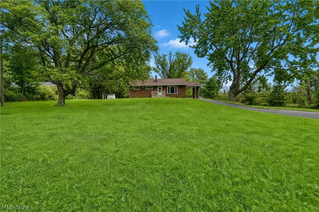 3864 State Road South Ashtabula, OH 44004 - Photo 5 of 50 Expansive grassy lot featuring mature trees, a paved driveway, and a brick exterior residence with a covered entryway