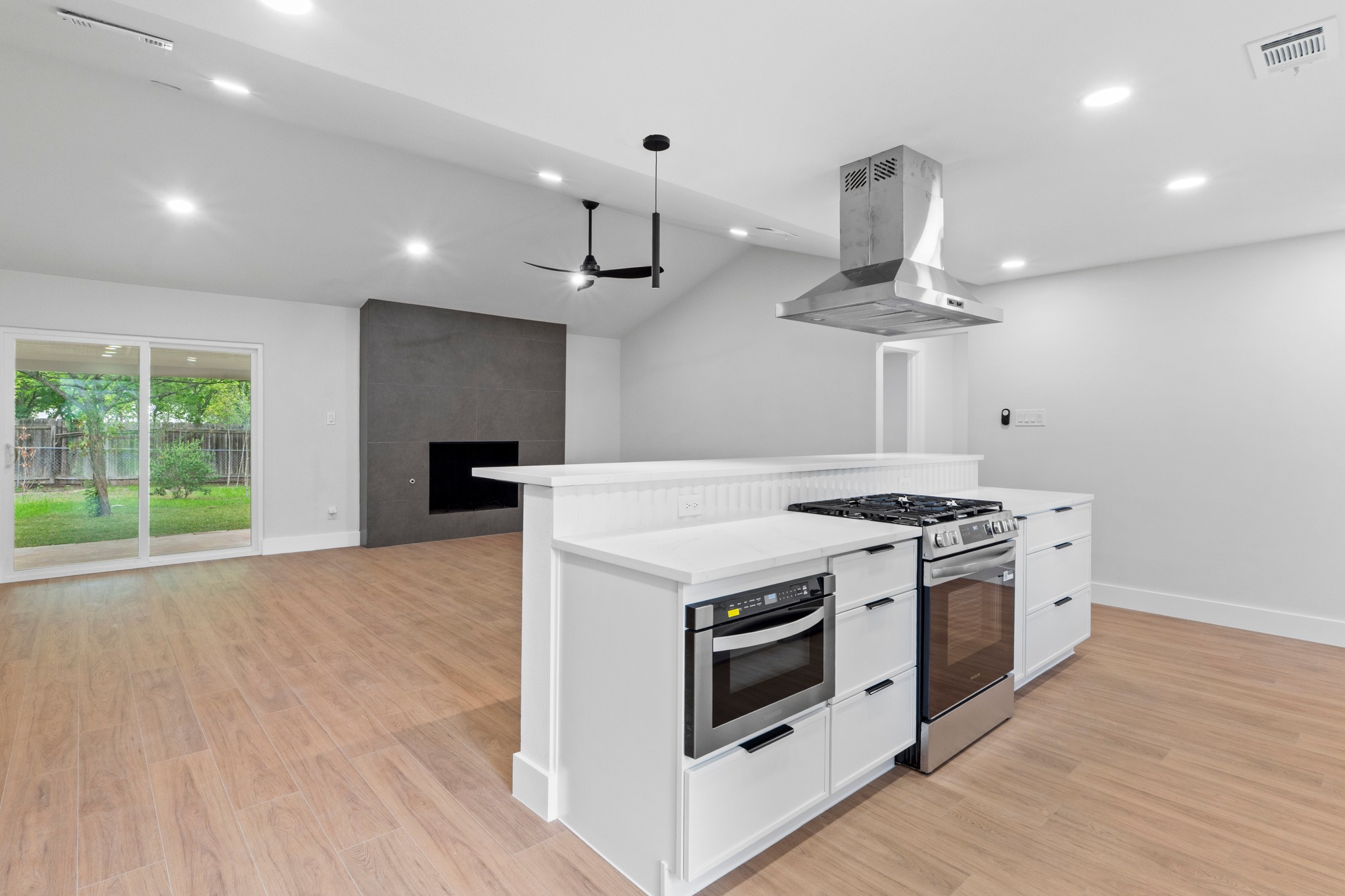 1608 Springer Lane Austin, TX 78758 - Photo 28 of 35 Open-concept kitchen and living area featuring a vaulted ceiling, wood-finish flooring, a contemporary fireplace, and a kitchen island with built-in stainless steel appliances