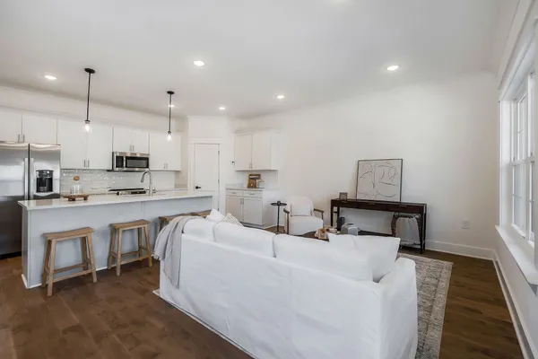 a living room with stainless steel appliances furniture a rug and a kitchen view
